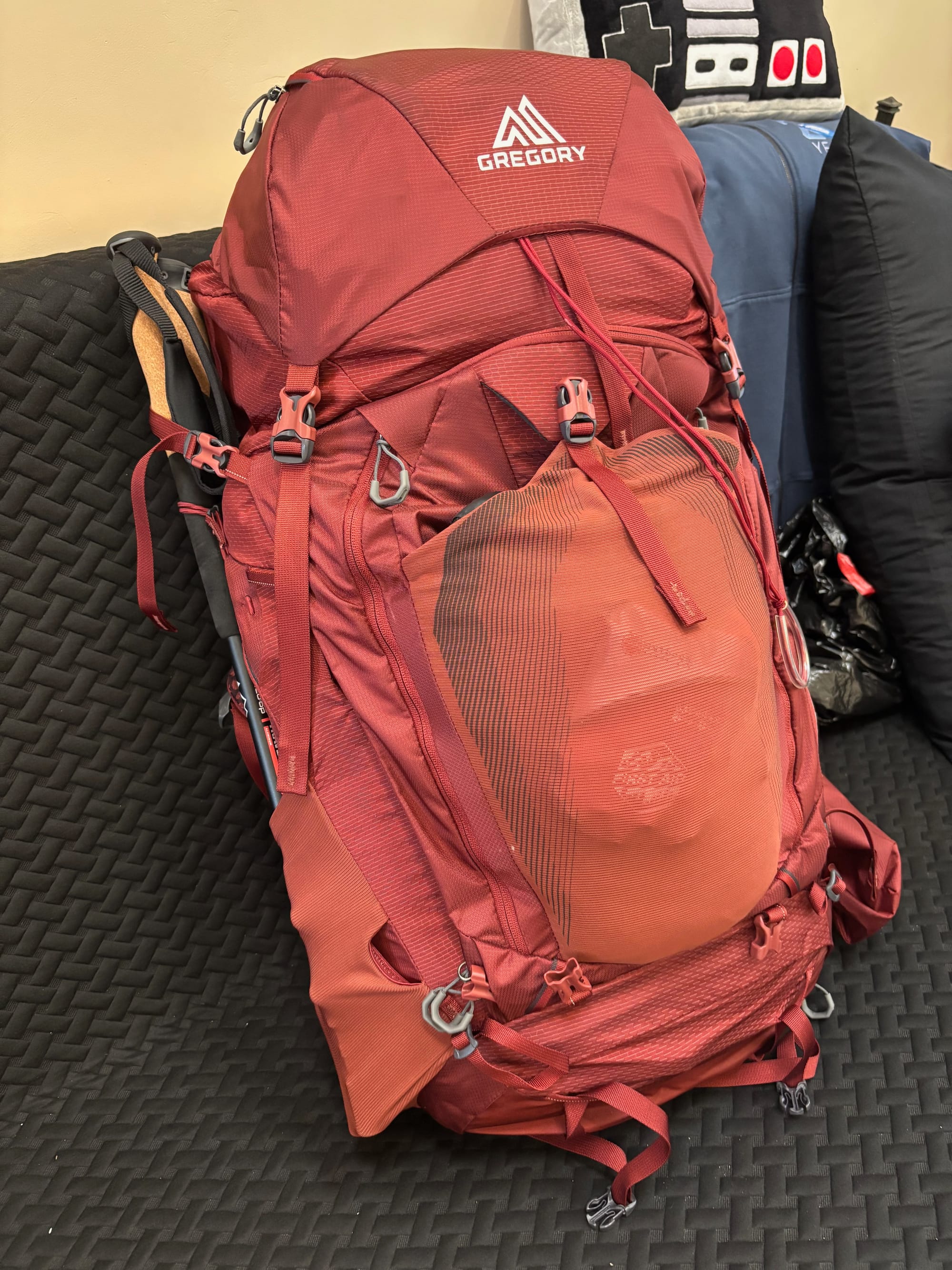 A large 65L Gregory backpack sitting on a black futon.