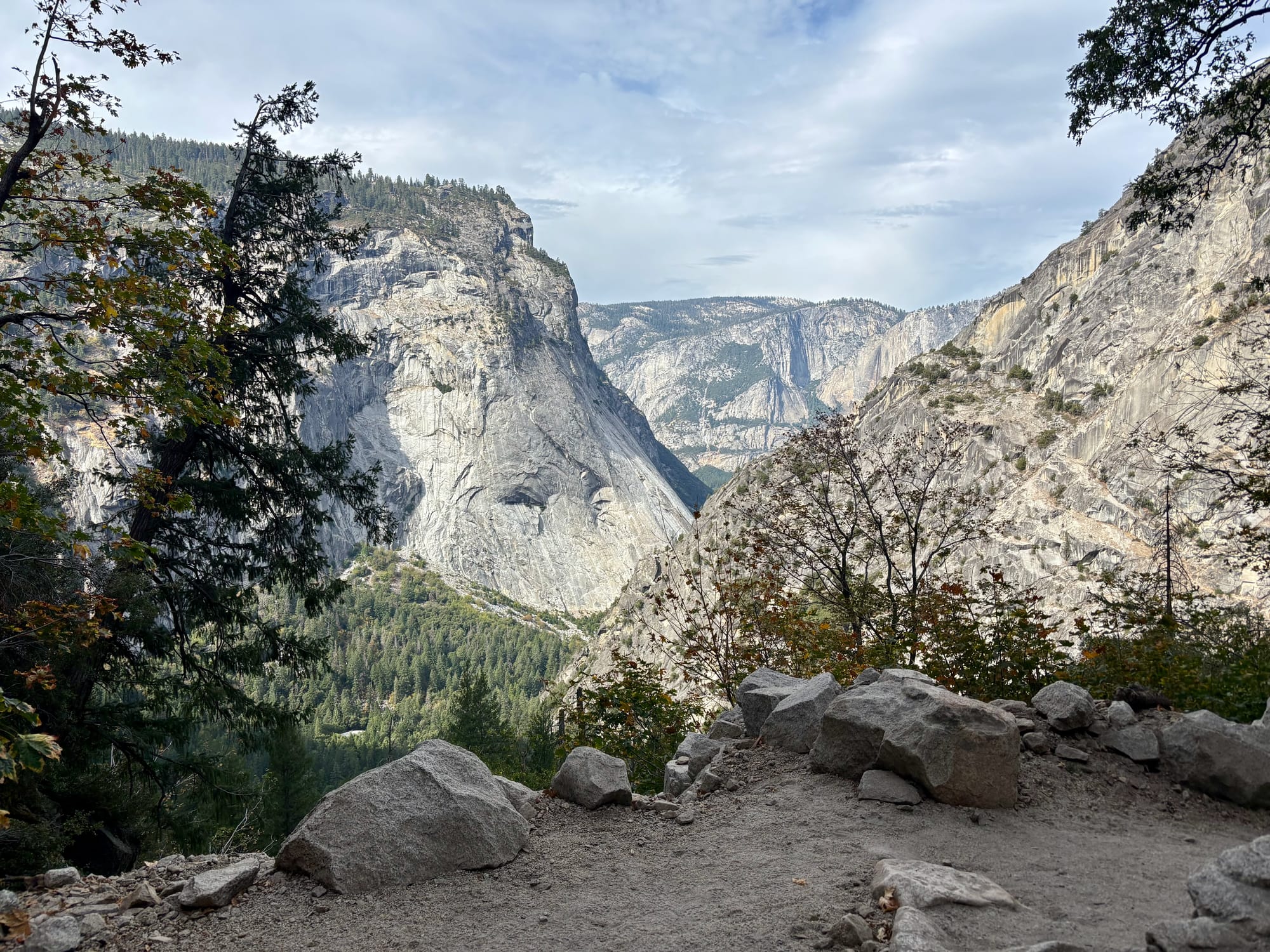 A scenic view of a mountainous landscape with rocky cliffs, trees, and a cloudy sky.