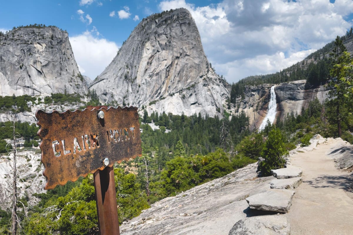 Mountainous landscape with a trail, a sign saying "Clark Point," and a distant waterfall.