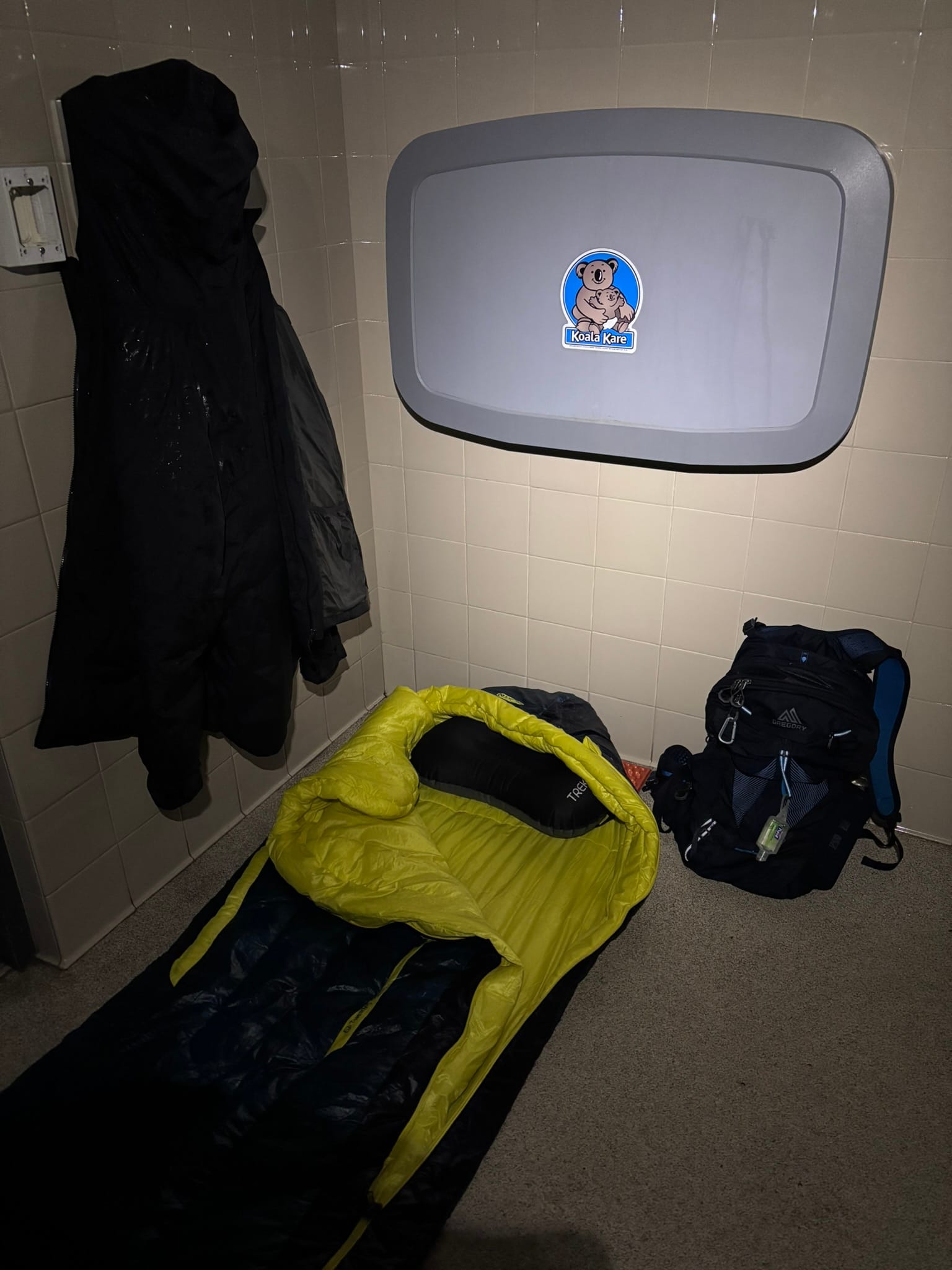 A blue and yellow sleeping bag laid out on a tiled floor next to a backpack.