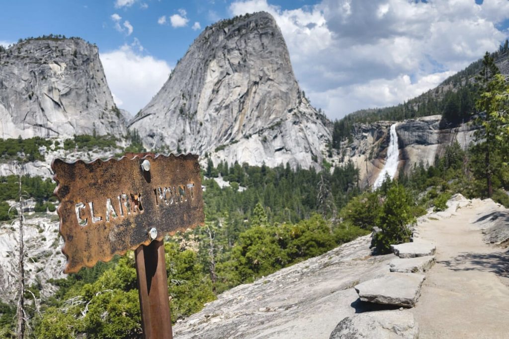 Mountainous landscape with a trail, a sign saying "Clark Point," and a distant waterfall.
