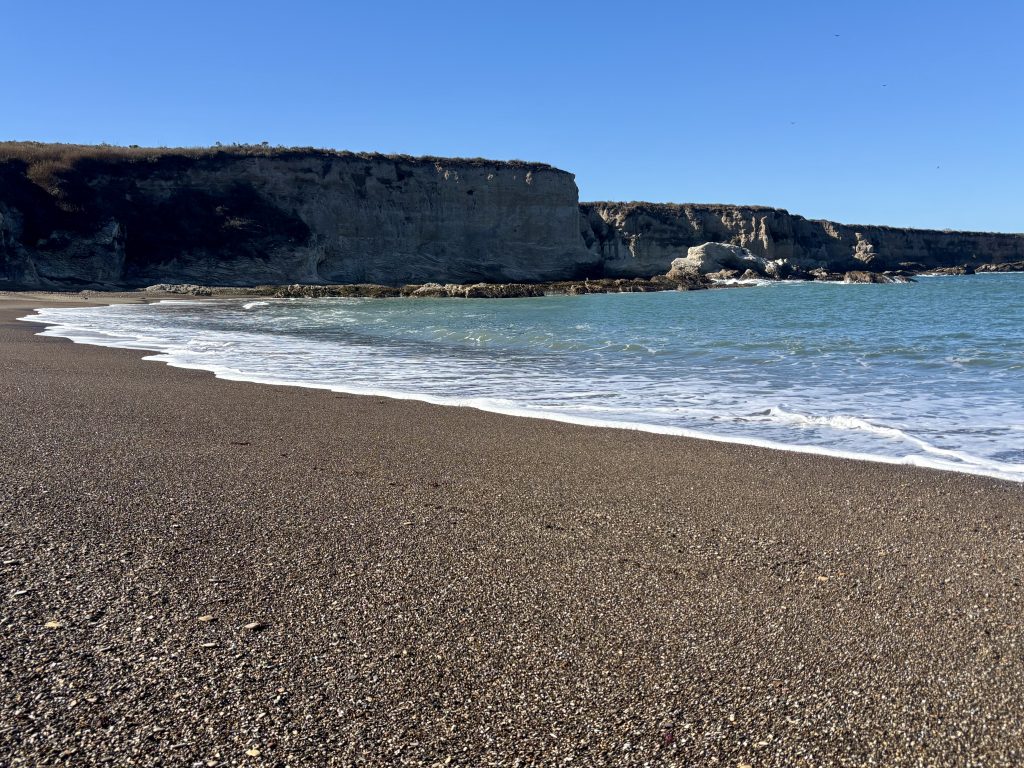 A rocky coastline with a dark, wave-worn cliff face meeting the turquoise water.