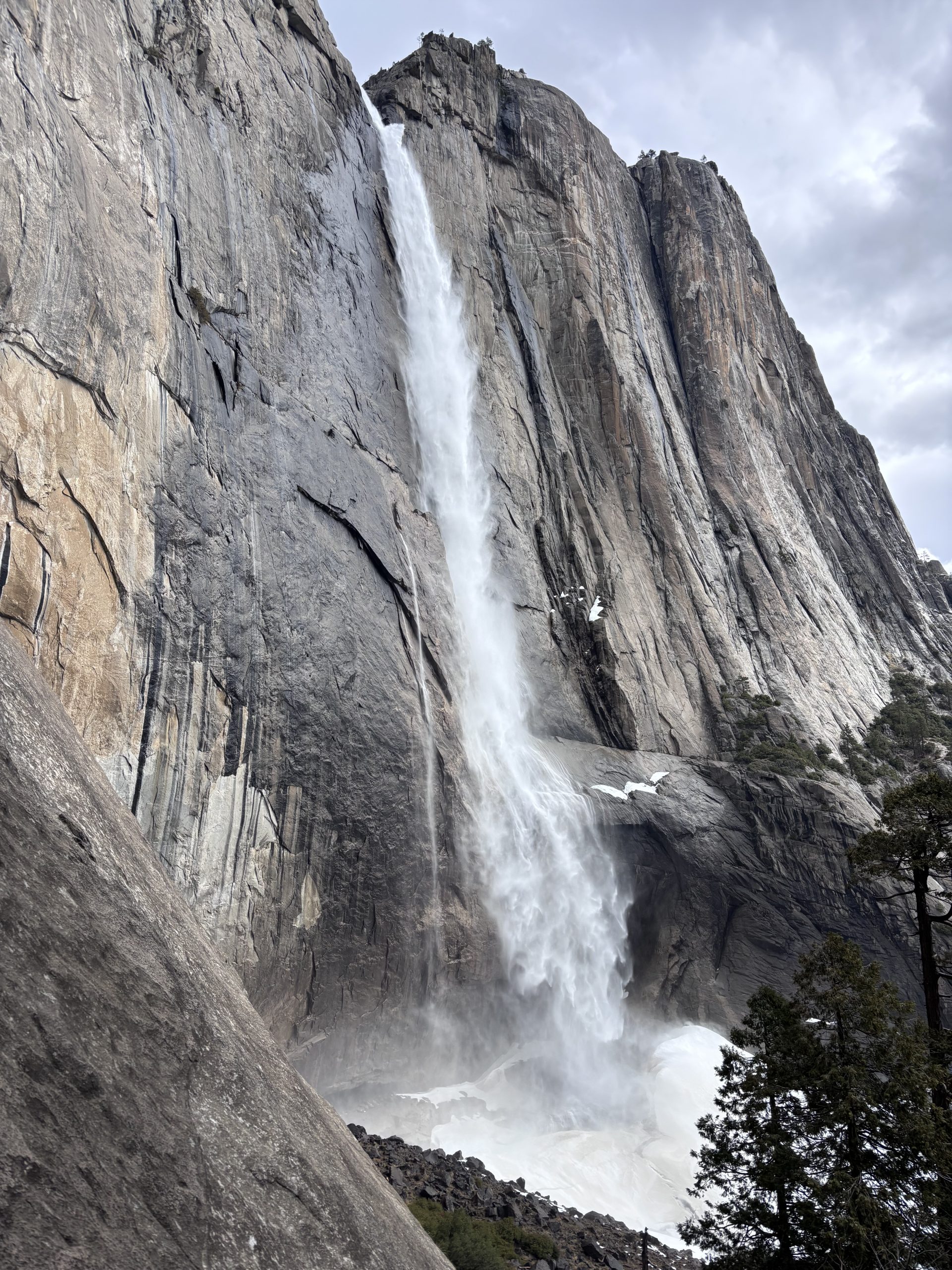 Tall waterfall plunging down a sheer granite cliff, with small patches of snow. 