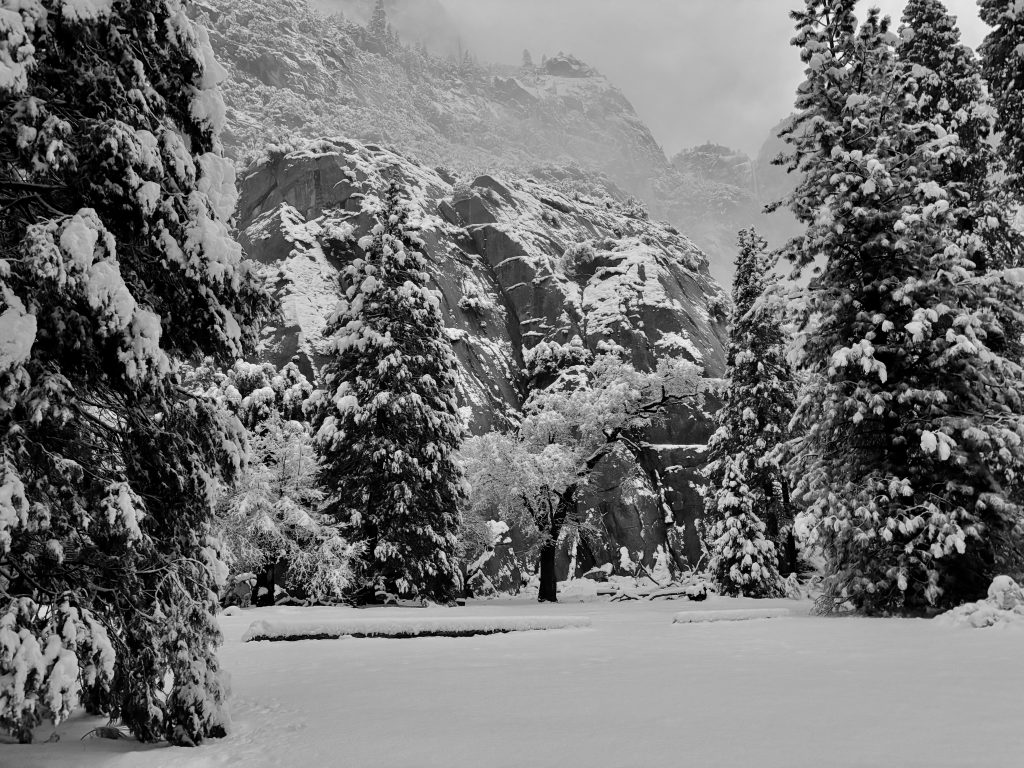 Wooden picnic table and benches covered in a thick layer of fresh snow at night.