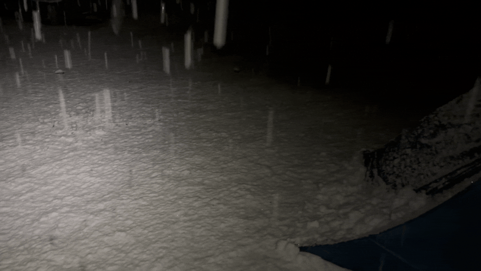 Heavy snow falls onto a blue tent and the surrounding ground.