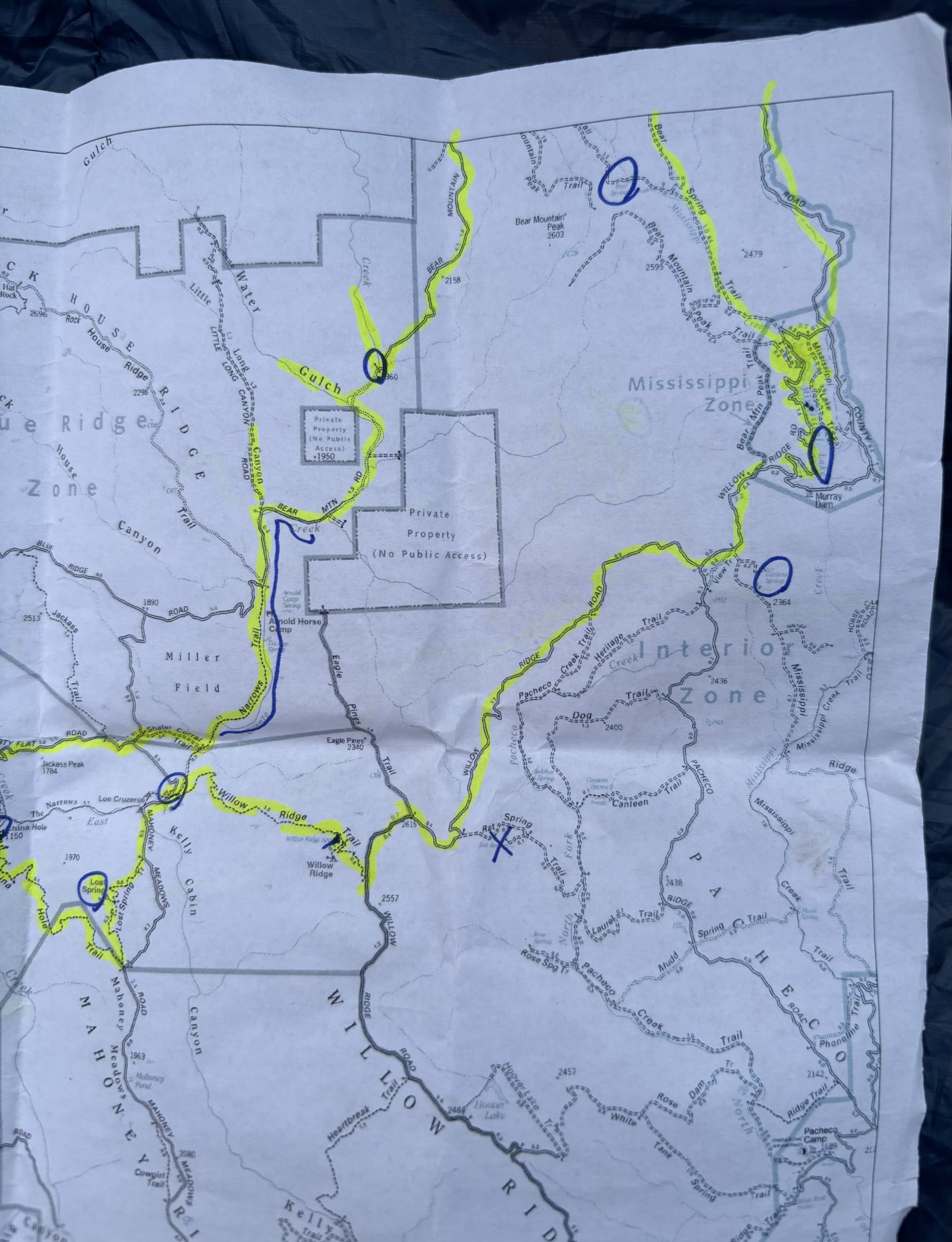 Folded paper map of Henry W. Coe State Park (Pine Ridge vicinity) with trails and routes highlighted in yellow and several sections circled in blue.