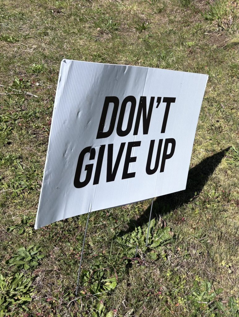 A white sign stuck into the ground says "DON'T GIVE UP" 
