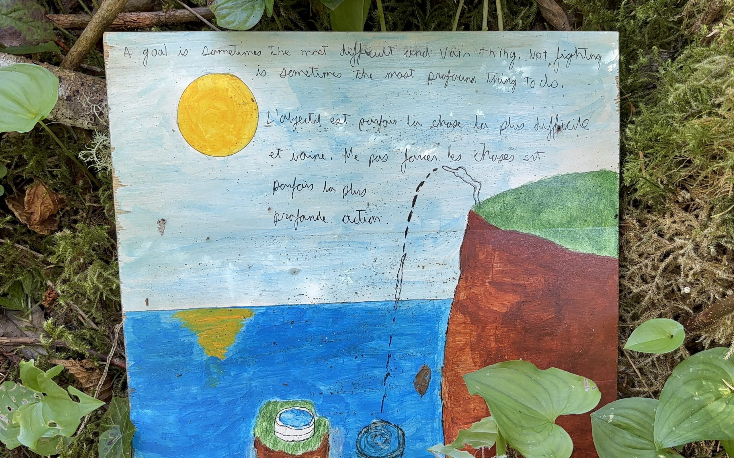 A square wooden sign lies nestled amongst green foliage and weeds. The sign is painted with a vibrant, stylized sunset scene over the ocean. A quote is written across the top, in English and French, reflecting on the value of perseverance.