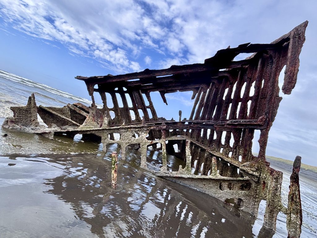 Rusting, skeletal remains of the Peter Iredale shipwreck embedded in the sand at Fort Stevens State Park, Oregon — iconic landmark on the Oregon Coast Trail.