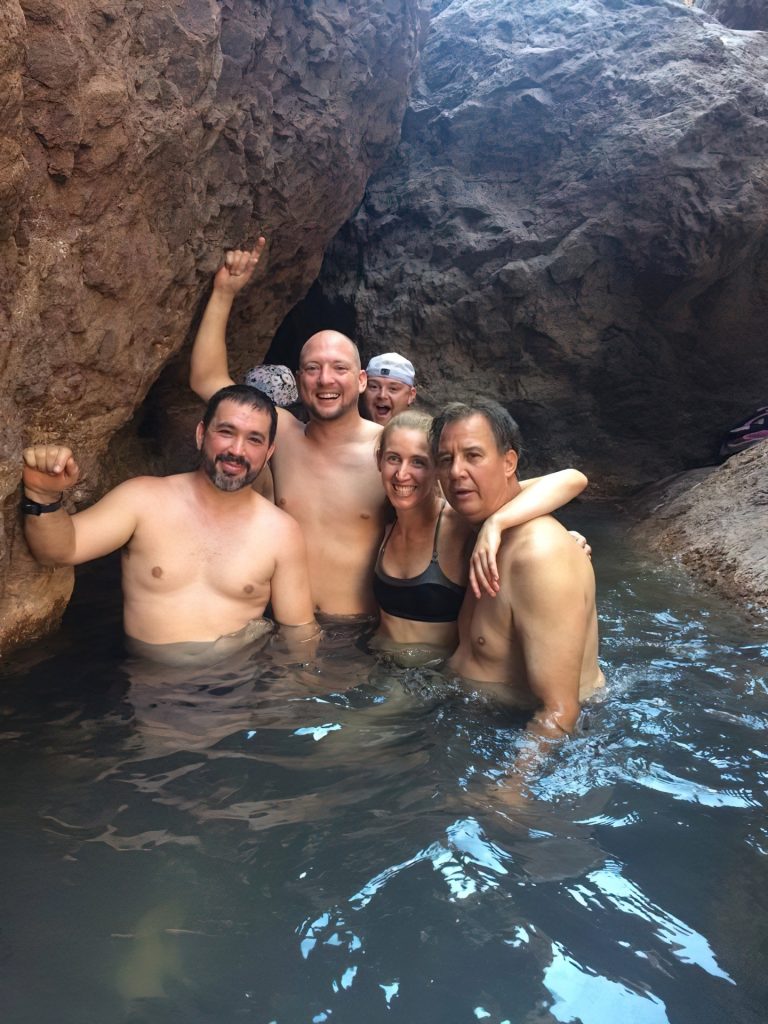 5 people smiling and posing in a rocky water hot spring.