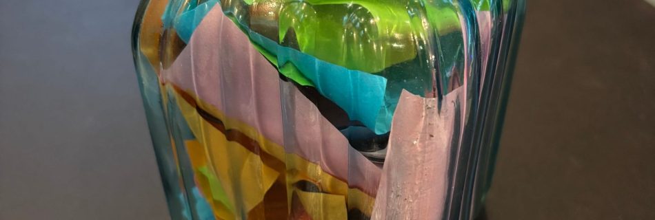 Glass jar filled with colorful folded paper notes, with a decorative metal lid beside it.